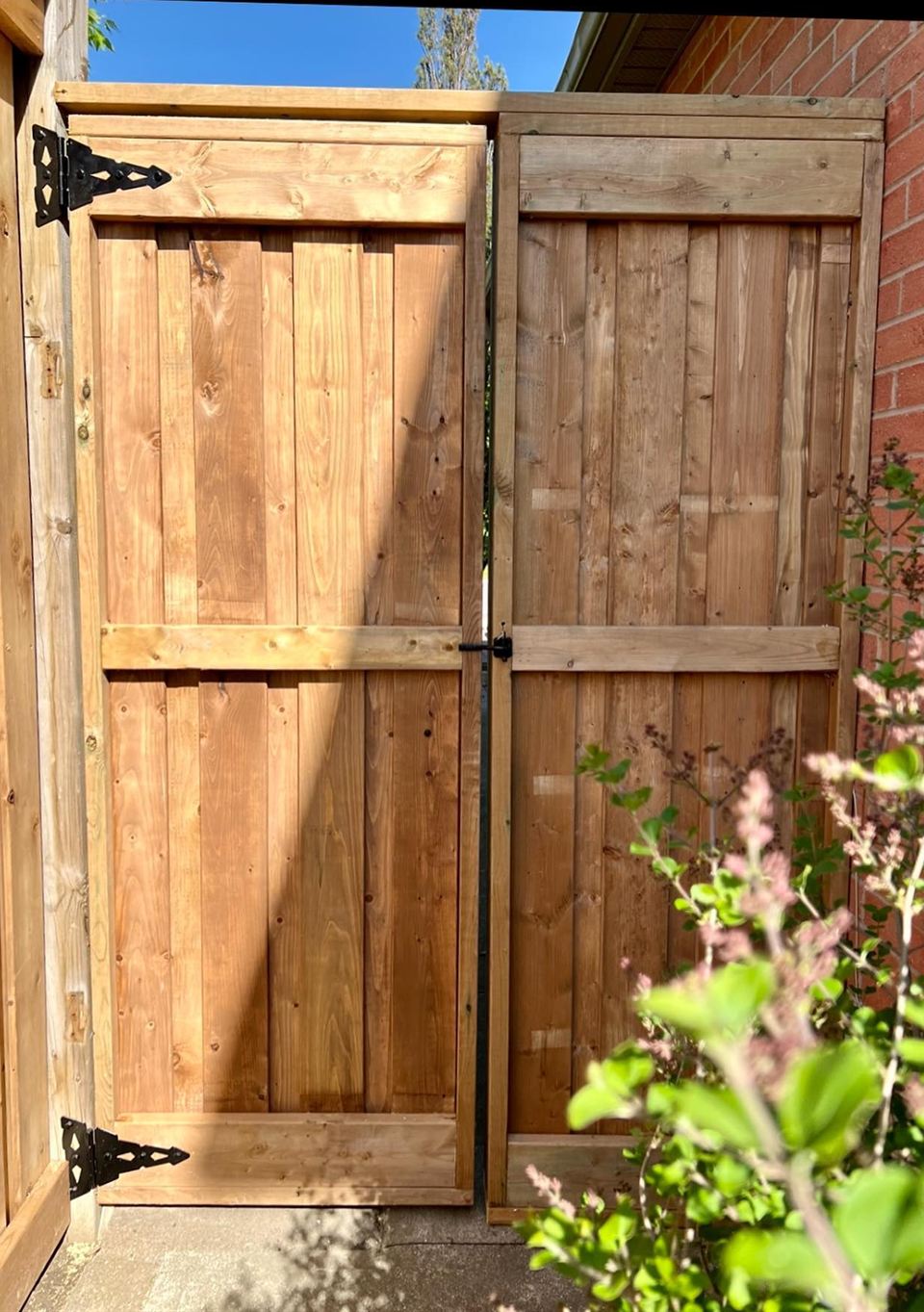 Yard side of the rebuilt side gate: cross-braced cedar panels on black strap hinges
